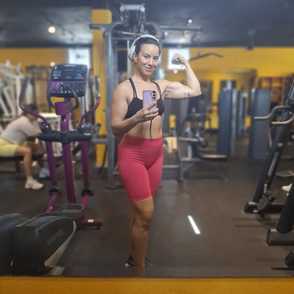 Gal Dorado flexing in a red training set in the gym mirror