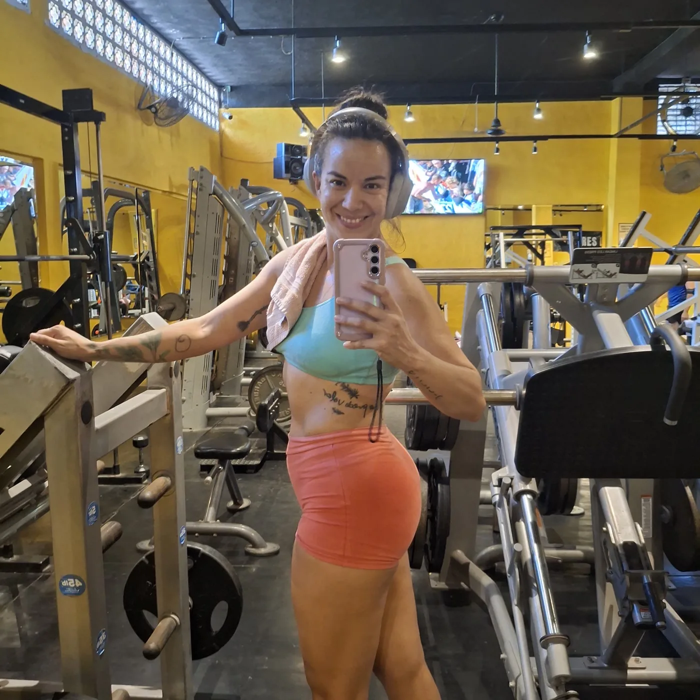 Gal Dorado smiling at the squat rack of her gym, towel over her shoulder, mid strength session